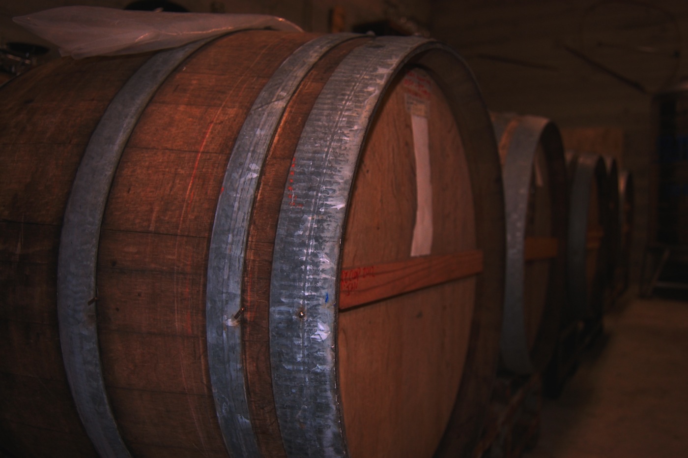 Close-up view of large wooden barrels with metal hoops, stored in a dimly lit cellar.